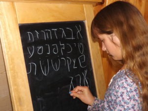 Girl writing aleph bet at chalkboard